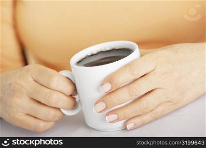 Mid section view of a senior woman holding a cup of black coffee