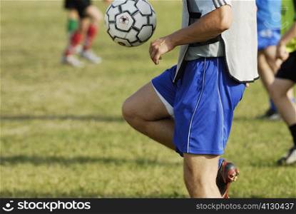 Mid section view of a soccer player balancing a soccer ball on his thighs