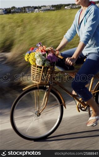 Mid section view of a woman carrying flowers in a basket on her bicycle