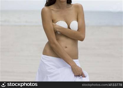 Mid section view of a woman covering her breasts with two seashells