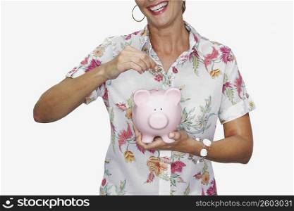 Mid section view of a woman holding a coin over a piggy bank and smiling