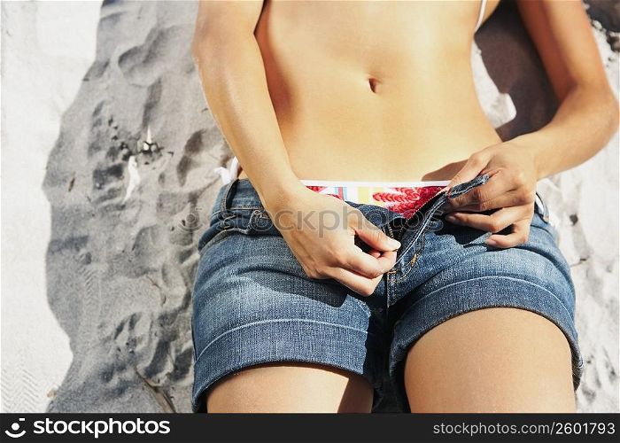 Mid section view of a woman lying on the beach and unzipping her shorts