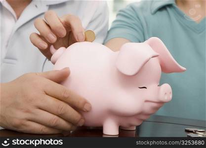 Mid section view of a woman putting a coin into a piggy bank held by a man