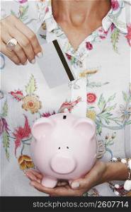Mid section view of a woman putting a coin into a piggy bank
