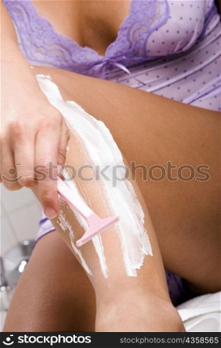 Mid section view of a woman shaving her leg with a razor