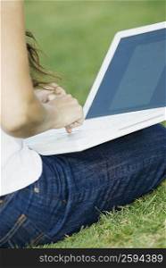 Mid section view of a woman sitting in a park and using a laptop