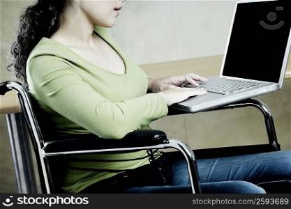 Mid section view of a woman sitting in a wheelchair and using a laptop