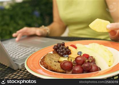 Mid section view of a woman using a laptop and eating fruit salad