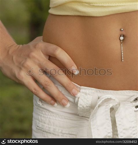 Mid section view of a woman with her hand on her hip and showing her pierced belly button