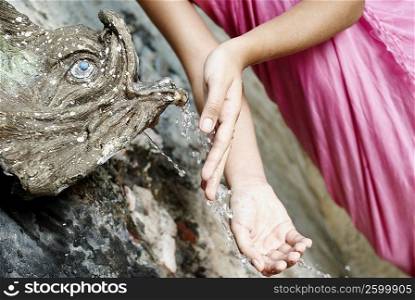 Mid section view of a woman with her hands under a fountain
