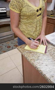 Mid section view of a woman writing on a notepad