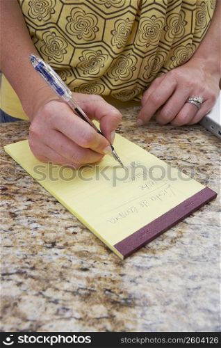 Mid section view of a woman writing on a notepad
