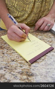 Mid section view of a woman writing on a notepad