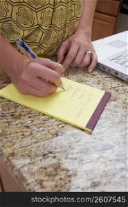 Mid section view of a woman writing on a notepad