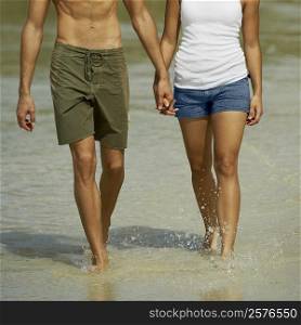Mid section view of a young man and a teenage girl holding hands and walking on the beach