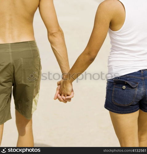 Mid section view of a young man and a teenage girl holding hands on the beach