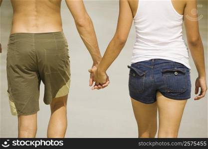 Mid section view of a young man and a teenage girl holding hands