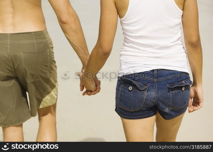 Mid section view of a young man and a teenage girl holding hands