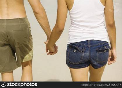 Mid section view of a young man and a teenage girl holding hands