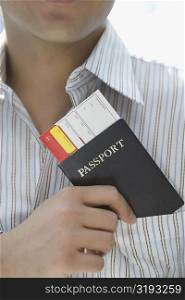 Mid section view of a young man putting a passport with an airplane ticket in his shirt&acute;s pocket