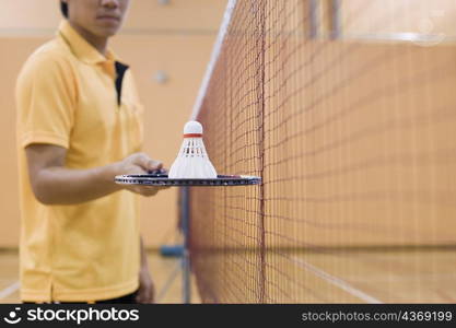 Mid section view of a young man standing in a badminton court and holding a badminton racket