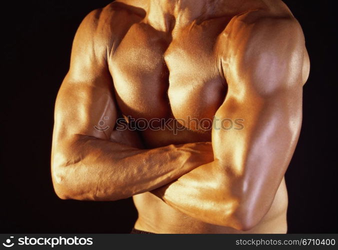 Mid section view of a young man standing with his arms folded