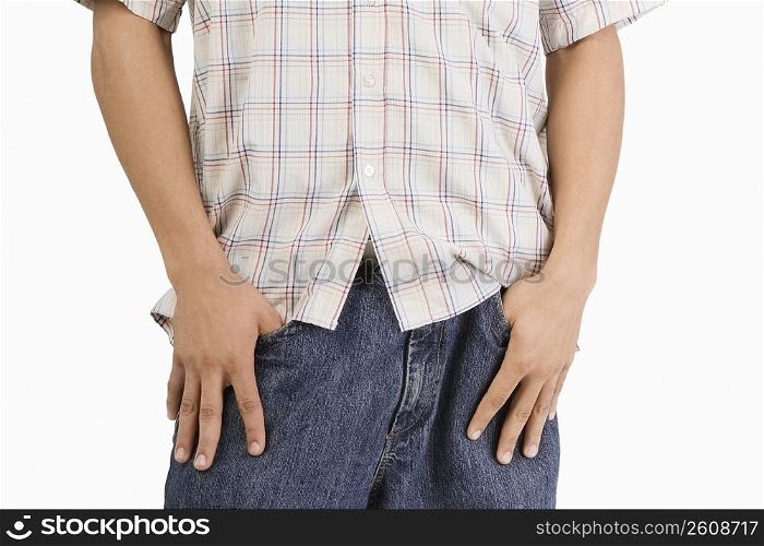Mid section view of a young man standing with his thumbs in his pockets