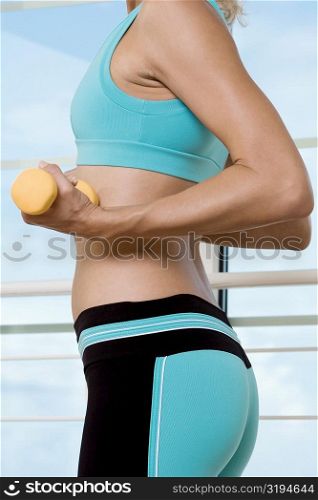 Mid section view of a young woman exercising with dumbbells