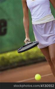 Mid section view of a young woman hitting a tennis ball with a tennis racket
