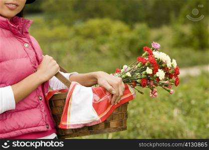 Mid section view of a young woman holding a basket of flowers