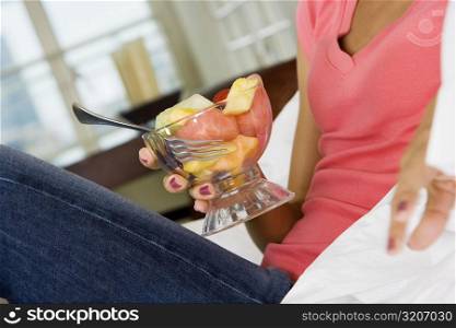 Mid section view of a young woman holding a bowl of fruit salad