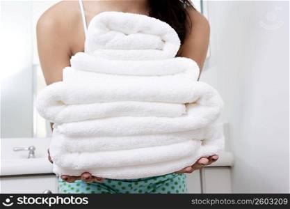Mid section view of a young woman holding a stack of towels