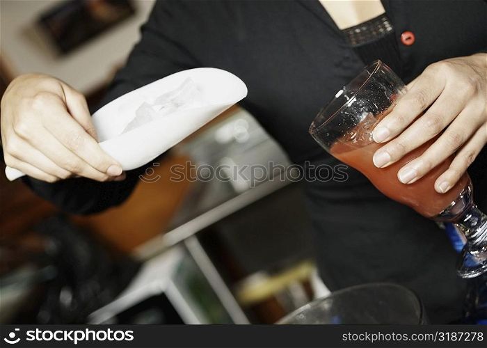 Mid section view of a young woman putting ice cubes into a glass with a scoop