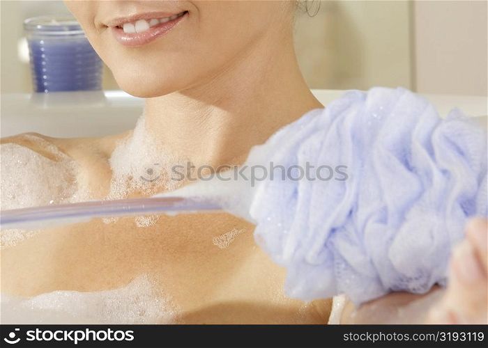 Mid section view of a young woman scrubbing her arm with a bath sponge