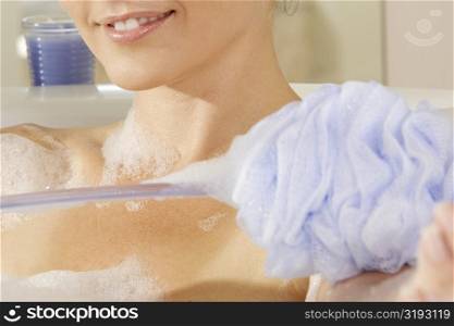 Mid section view of a young woman scrubbing her arm with a bath sponge