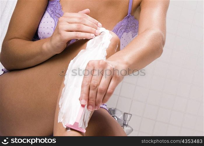 Mid section view of a young woman shaving her legs