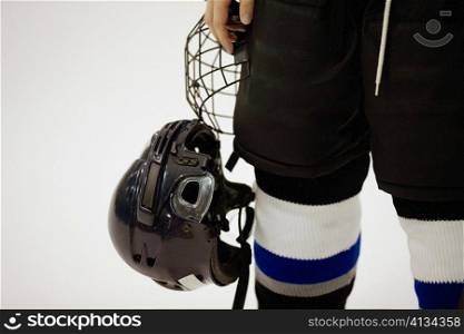 Mid section view of an ice hockey player holding a helmet