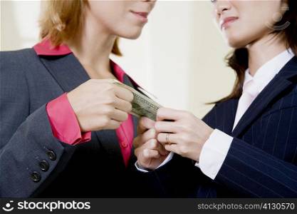Mid section view of two businesswomen holding a dollar bill