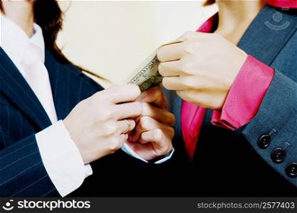 Mid section view of two businesswomen holding a paper currency note
