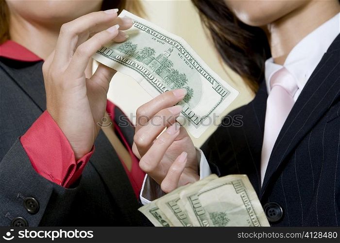 Mid section view of two businesswomen holding dollar bills
