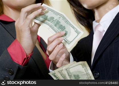Mid section view of two businesswomen holding dollar bills