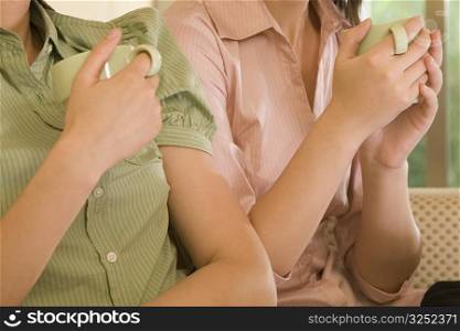 Mid section view of two women holding coffee cups