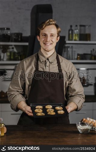mid shot chef holding tray with cookies