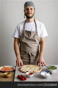 mid shot man standing near baked pizza dough with ingredients