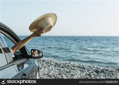 mid shot woman hand out car window holding hat near sea . Resolution and high quality beautiful photo. mid shot woman hand out car window holding hat near sea . High quality and resolution beautiful photo concept