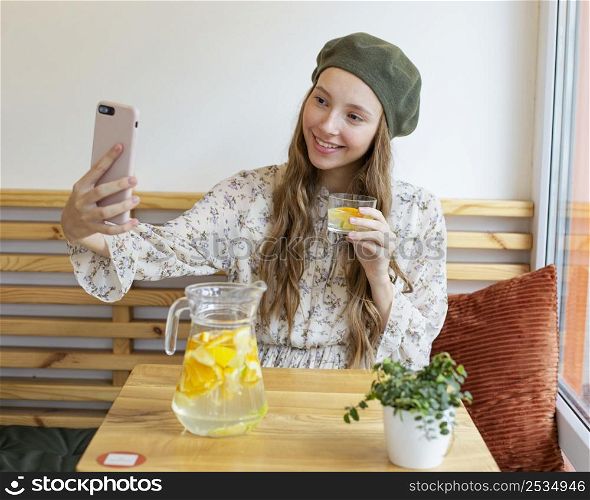 mid shot woman sitting table holding lemonade glass taking selfie