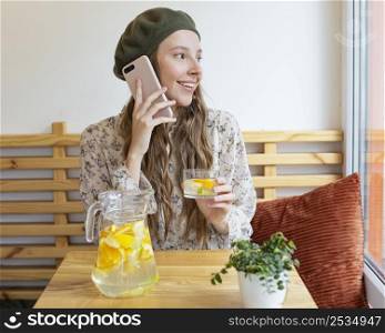 mid shot woman sitting table holding lemonade glass talking phone