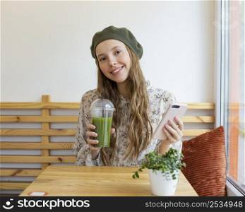 mid shot woman sitting table holding smoothie phone