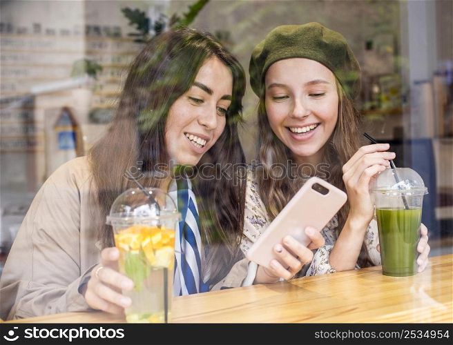 mid shot women with fresh juices cafe looking phone