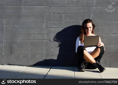 Middle-age businesswoman working with her laptop computer sitting on the floor outdoors.. Young businesswoman working with her laptop computer sitting on the floor.